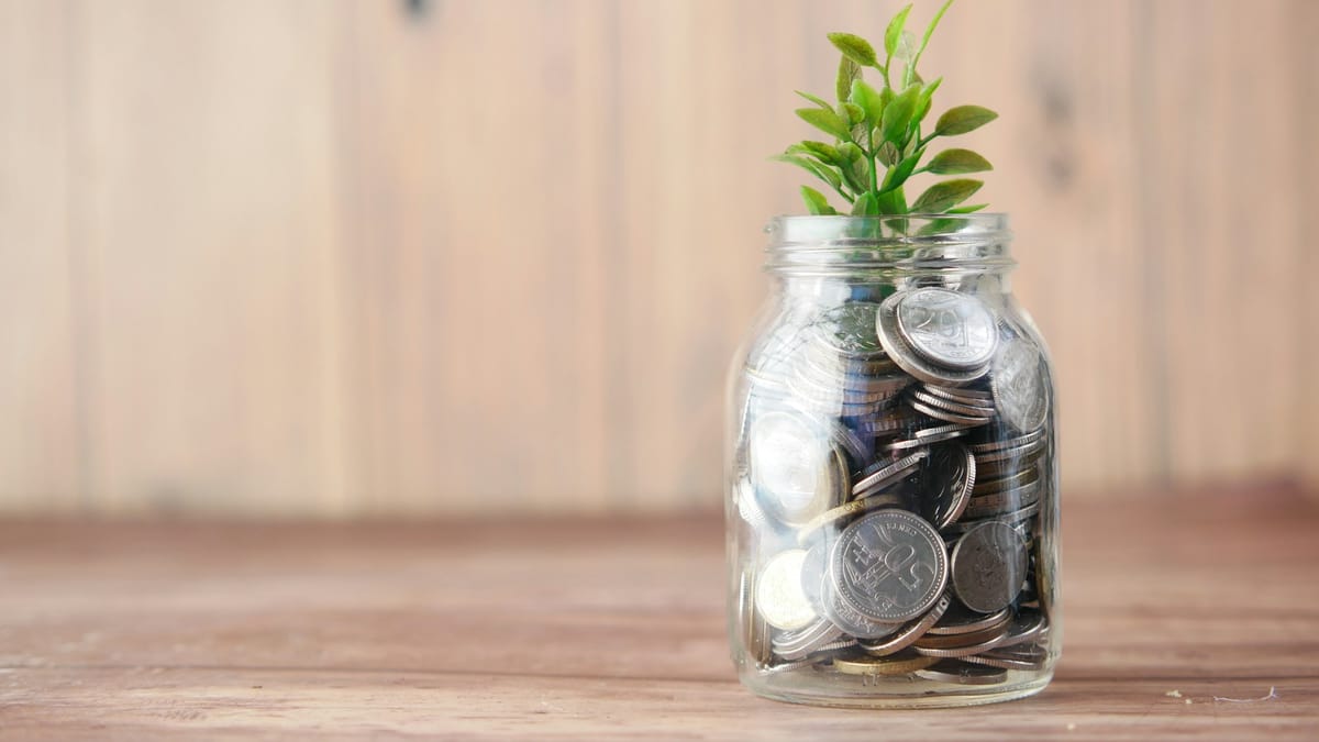 A glass jar filled with coins with a small plant growing from it, savings building up